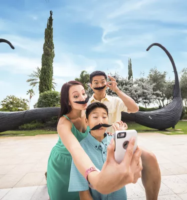 An Asiatic family wearing fake mustaches taking a selfie in front of the famous mustache sculpture at the Dali museum in St. Pete.