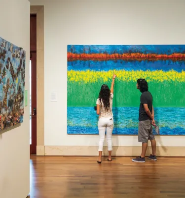 Ein Paar schaut sich ein Gemälde im St. Pete Museum of Fine Arts genau an.