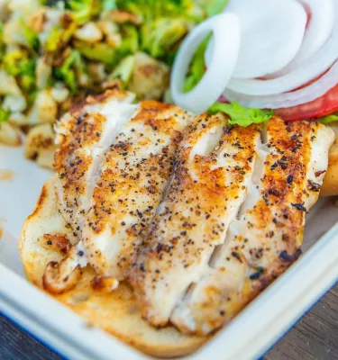 A close view of a grouper fish plate with onions, tomatoes and green vegetables.