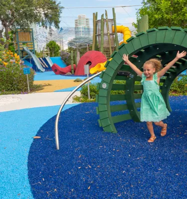 A little girl dressed in green dress, with arms wide open while going through a tunnel at St. Pete Pier playground.