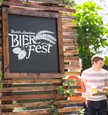 A man and woman at a cocktail table with the Busch Gardens Bier Fest sign in the background