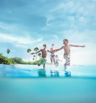 Three children play in the ocean in front of an island.