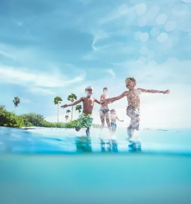 Three children play in the ocean in front of an island.