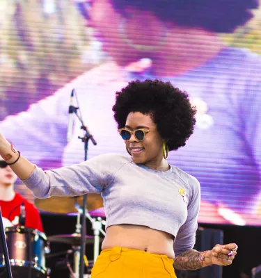Woman stands on stage holding a microphone stand while a drummer plays behind her.