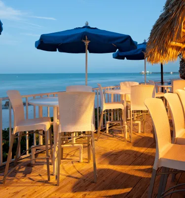 A waterfront deck with tables and umbrellas at dusk at Mangos DoubleTree Beach Resort by Hilton Tiki Bar