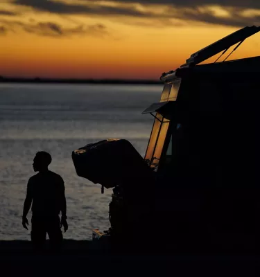 Man standing outside watching the beach during evening sunset. Featuring yellow sunset skies and a food truck.