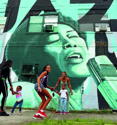 Children and parents playing outside in front of a wall mural in the Deuces Live district during the day.