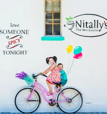 Colorful painting on a white wall of two kids riding a pink bike with balloons on the back