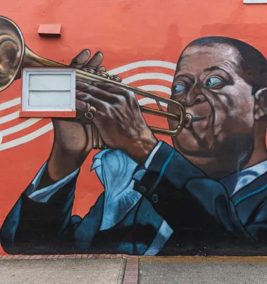 A mural by Herbert Davis in South St. Pete on a red background depicts Louis Armstrong playing the trumpet