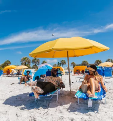 um casal relaxa em espreguiçadeiras sob um guarda-sol amarelo brilhante nas areias brancas da Madeira Beach