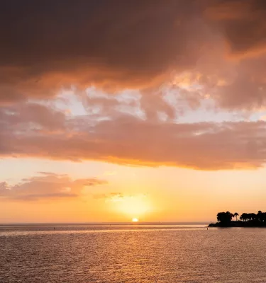 a sky at sunset with yellow and pink colors and a large cloud formation, water is in the foreground with land can be seen at the right