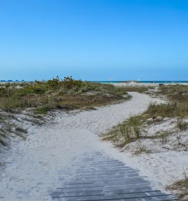 um calçadão arenoso leva a um caminho de areia ladeado por dunas e vegetação no Sand Key Park