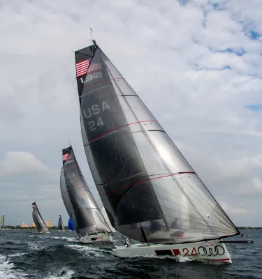 Large grey sailboat in the ocean featuring the American flag with other sailboats on the horizon.
