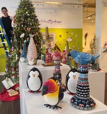 Woman standing on a ladder in Florida CraftArt store featuring a Christmas Tree and other holiday decor.