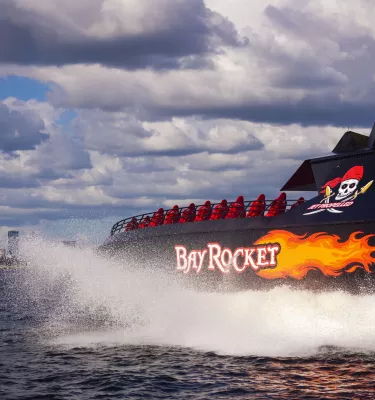 Photo of the Tampa Bay Rocket Boat splashing on the water. It has red seats and orange flame detailing on the side of the boat.