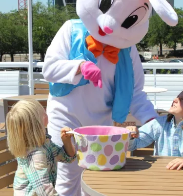 Easter bunny passing out eggs to two kids on a cruise during the day.