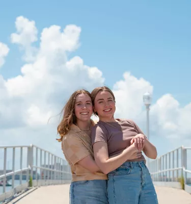 two women embrace and pose for the camera on the waterfront in Gulfport FL