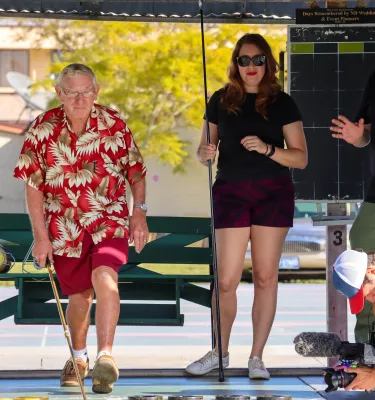 a man in a red hawaiian shirt and shorts plays shuffleboard with several other people