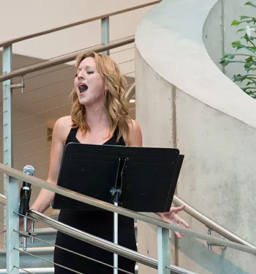 Blonde woman singing opera on the stairs to a crowd of people at the Dali Museum.