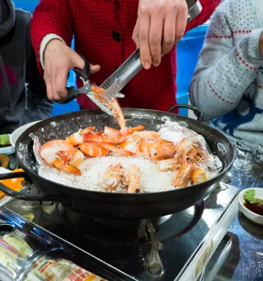 Photo of a man cooking seafood outside in a large black pan.