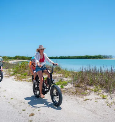 Familia en ebikes paseos por un camino de arena junto al agua