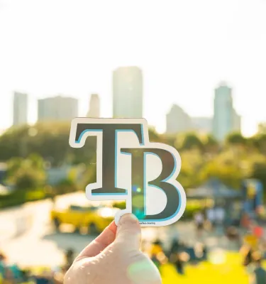 Tampa Bay Rays logo held up against St. Pete skyline