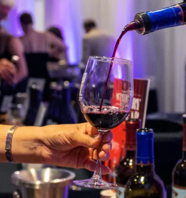 Woman holding a glass of wine while bartender pours her a red glass.