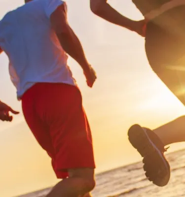 Two people running on the beach with the sunset behind them.
