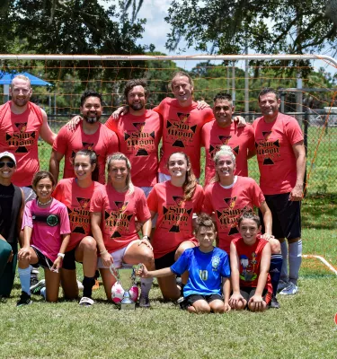 Photo of a soccer team in red uniforms smiling at the camera in front of the goal.