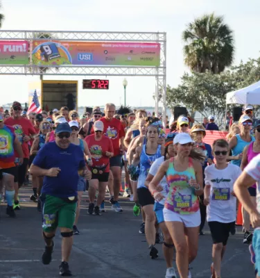 Multiple people running outside by the water in the Hippie Dash race in Safety Harbor, FL.