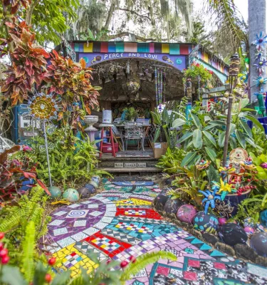 Bunte Mosaikfliesen führen zu einem „Peace and Love“-Baldachin im Garten von Whimzeyland in Safety Harbor, Florida
