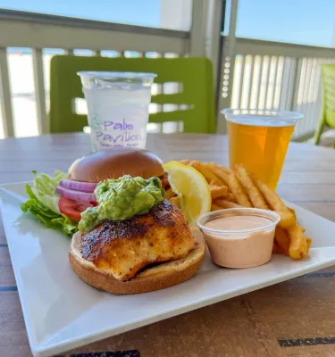 a blackened grouper sandwich with guacamole on top on a brioche bun with fries and a beer at Crabby's Beachside Pavilion in Clearwater Beach