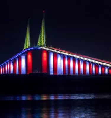 Image of the Skyway Bridge in St. Pete, FL at night with blue, red and white lights under it.