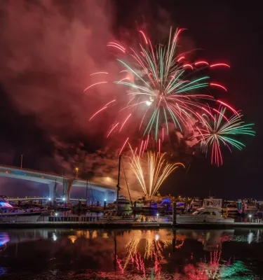 Red and green fireworks exploding in the night sky in Clearwater, FL over a bay of water.