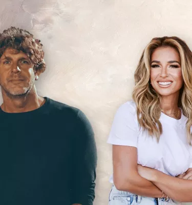 Musicians Billy Currington and Jessie James Decker standing in front of a white background smiling at the camera.