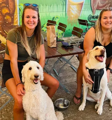 Two women hold their dogs on a brewery patio