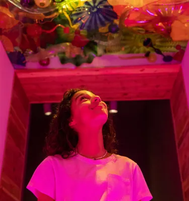 a person in a pink shirt walks underneath a ceiling made of art glass at The Chihuly Collection