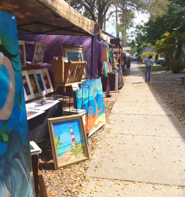 Tents filled with paintings and other artwork for sale line a sidewalk.