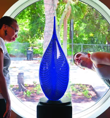 A woman and man look at a tall blue glass sculpture.