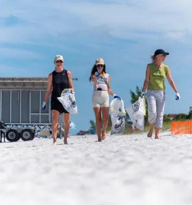 three women with trash bags at a beach clean up