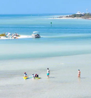 People wade in clear water with two islands nearby.