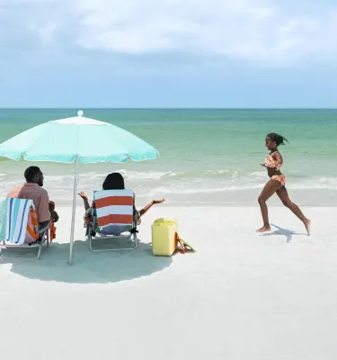 Girl running on the beach toward parents under an umbrella
