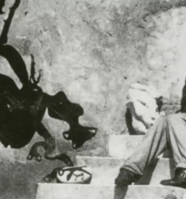Black and white photo of a woman sitting on stone steps with a black abstract figure next to her.