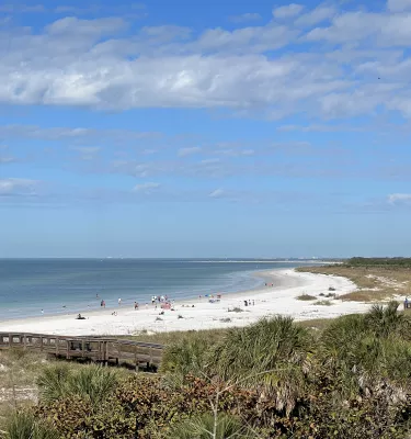 Photo of a beach during the day with blue skies, white sand and green trees.