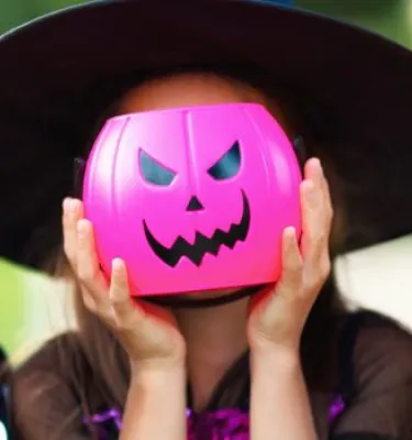 Three children dressed up for halloween holding up plastic pumpkins in front of their faces.