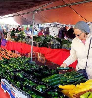 Outside beach farmers market showing a woman shopping for produce items that are on a long red table.