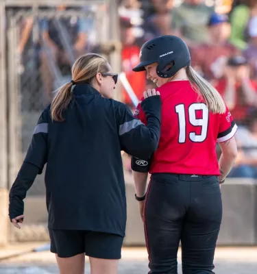 Female softball coach walking with a player in a red jersey.