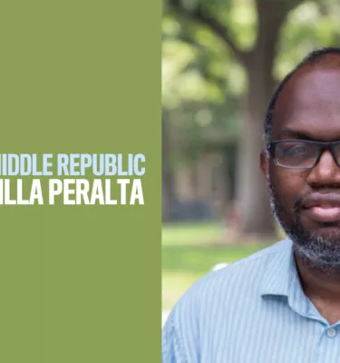 African-American man wearing glasses looking at the camera wearing a blue button-down shirt outside.