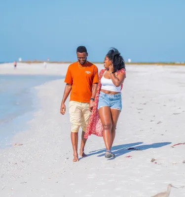 a young couple in casual clothes walking on a white sand beach