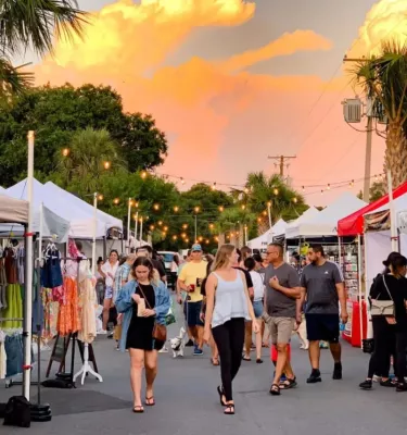 Outside sunday market in St. Pete featuring multiple white vendor tents and groups of people shopping and walking around.